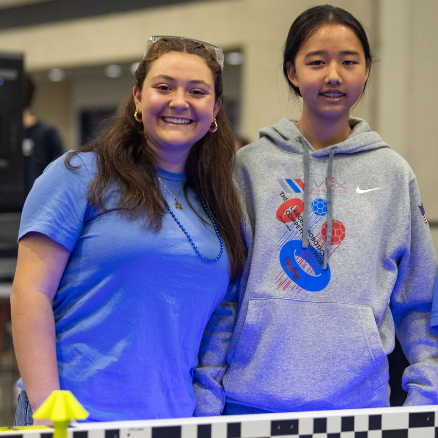 Two students pose at the VEX Robotics World Championship, the participant on the right wears VEX Robotics World Championship apparel