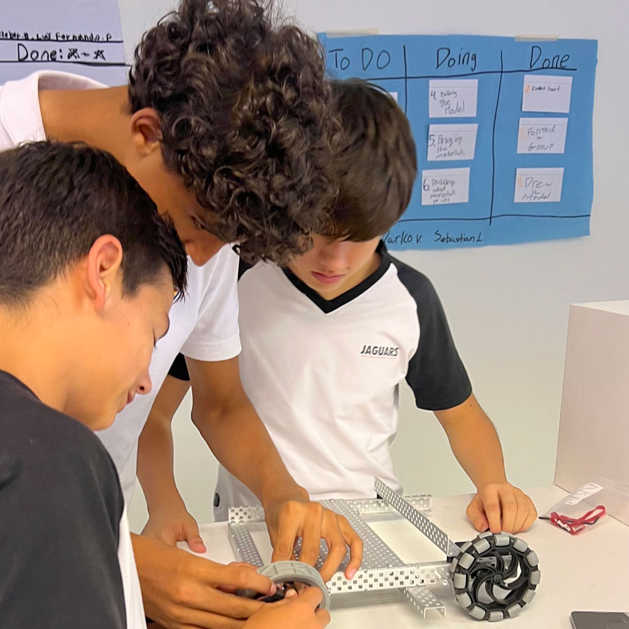 Three robotics students work on their robot on a classroom